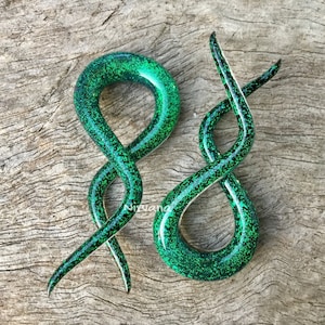 May include: A pair of green glass spiral ear gauges with a glittery finish. The gauges are shaped like a snake and have a hole in the center for the ear.