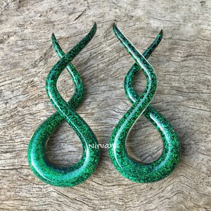 May include: A pair of green glass ear gauges with a sparkly finish. The gauges are shaped like an infinity symbol and are twisted.
