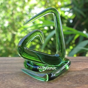 May include: A green glass ear cuff in the shape of a triangle with a smaller triangle inside. The ear cuff is on a wooden surface. Nirvana is written on the ear cuff.