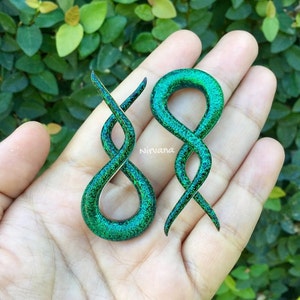 May include: A pair of green and black spiral ear gauges with a glitter finish. The gauges are made of wood and have a unique, twisted design.