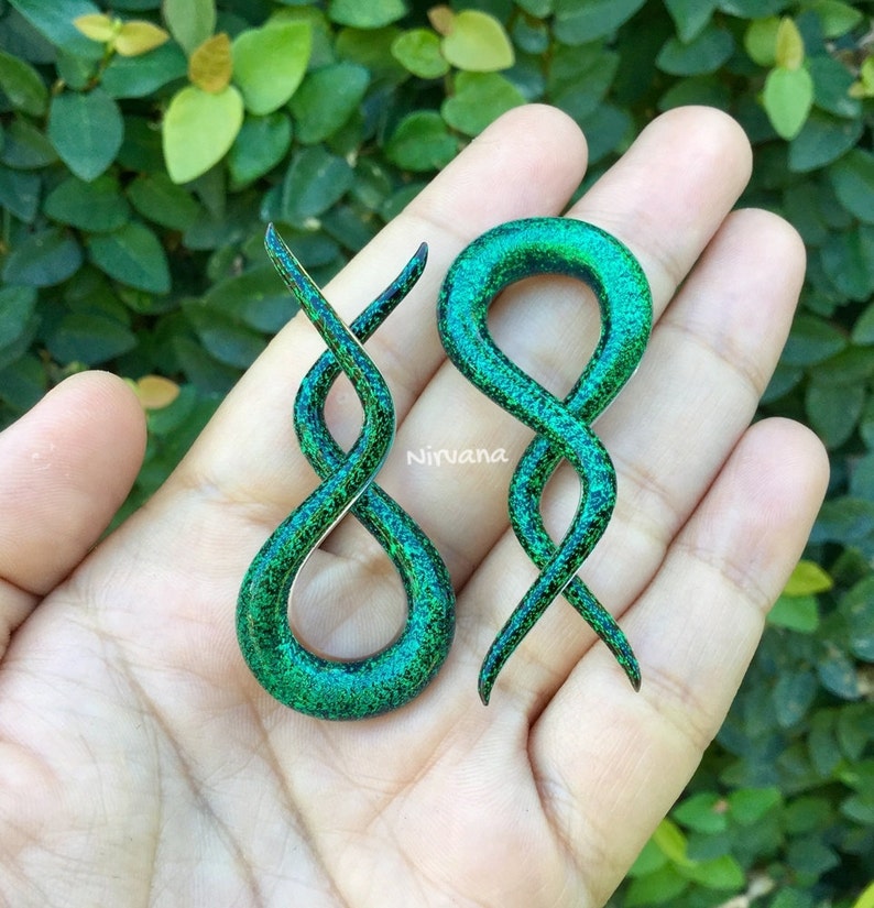 May include: A pair of green and black spiral ear gauges with a glitter finish. The gauges are made of wood and have a unique, twisted design.