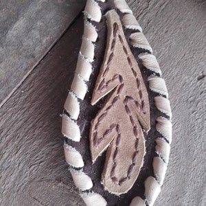 Peut inclure: Un porte-clés en cuir marron avec une bordure en cuir blanc et un motif de plume cousu.