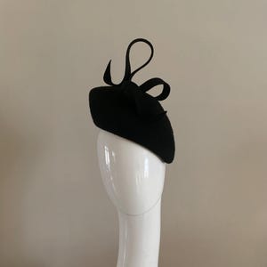 Black wool felt perching hat adorned with a sculptured ribboned loop detail.