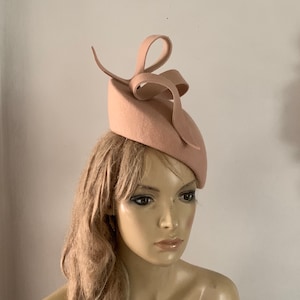 Beige wool felt perching hat adorned with a sculptured ribbon detail.