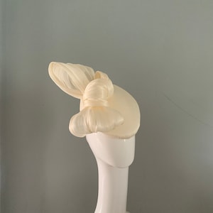 Cream silk perching beret hat adorned with a sculptured bow.
