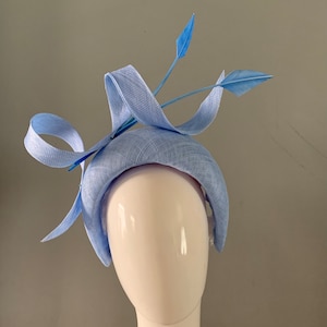 Puede incluir: Una diadema azul claro con un gran lazo y dos plumas. La diadema está hecha de un tejido suave y texturizado.