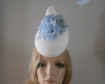 white sinamay 3d "pod" perching hat adorned with powder blue& grey silk roses,pierced with a dramatic arrowhead feather detail