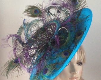 Large saucer hat in teal adorned with purple and green peacock eyes & swords.