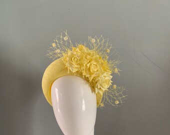 Fascinator con cappello appollaiato a corona gialla ornato con fiori di seta e velo da vedova allegra.