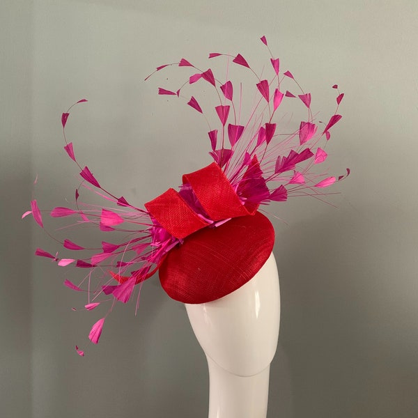 Béret perché en sinamay rouge avec boucles sculptées, fleurs fuchsia soyeuses, détails de plumes coupées à la main.