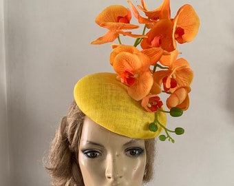 May include: A yellow fascinator hat with a cluster of orange orchid flowers.