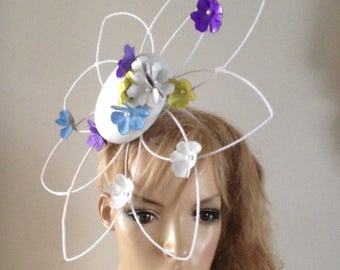 chic white leather button fascinator hat centred on a lattice sculpture adorned with purple,turquoise yellow & white leather flowers.