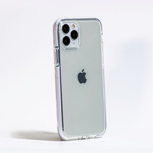 May include: A clear phone case with a white border, protecting a silver iPhone with a black Apple logo. The phone has a triple lens camera system.