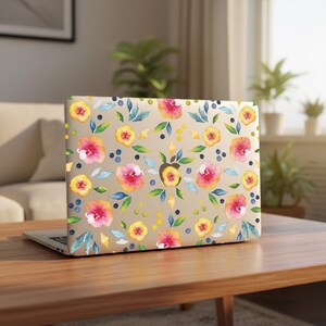 May include: A laptop computer featuring a beige skin with a repeating watercolour pattern of pink and yellow flowers, green leaves, and small blue berries. The design covers the entire lid, showcasing a vibrant floral motif on a neutral background.