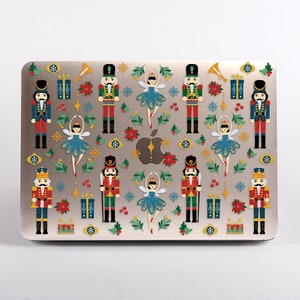 May include: A laptop computer with a colourful design featuring nutcracker soldiers and ballerinas. The design includes red, green, blue, and gold colours. The laptop has a silver finish.