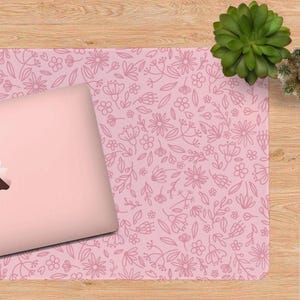 K&ouml;nnte beinhalten: Ein pinkfarbener Laptop liegt auf einer passenden pinkfarbenen Schreibtischunterlage. Die Unterlage hat ein zartes Blumenmuster in einem helleren Rosaton. Daneben steht eine gr&uuml;ne Sukkulentenpflanze auf einer Holzoberfl&auml;che.