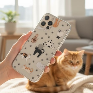 May include: Clear phone case featuring various cat illustrations in different colors and patterns, including a black cat, a Siamese cat, and a calico cat. The case also has paw print designs.
