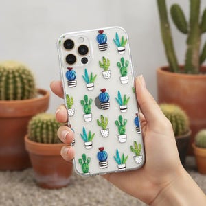 May include: Clear phone case featuring a repeating pattern of illustrated cacti in white pots. The cacti are in shades of green, blue, and red. The case is held in a hand, with several potted cacti in the background.