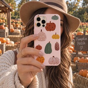 May include: A light pink smartphone case featuring a repeating pattern of various pumpkins in shades of orange, green, brown, and cream. The pumpkins have different shapes and textures, including solid colors and dotted designs, covering the back surface.