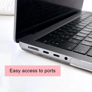 May include: A silver laptop with a black keyboard and a clear protective case. The side of the laptop features a magnetic charging port, two USB-C ports, and a headphone jack. A pink rectangular graphic with the text Easy access to ports is visible.
