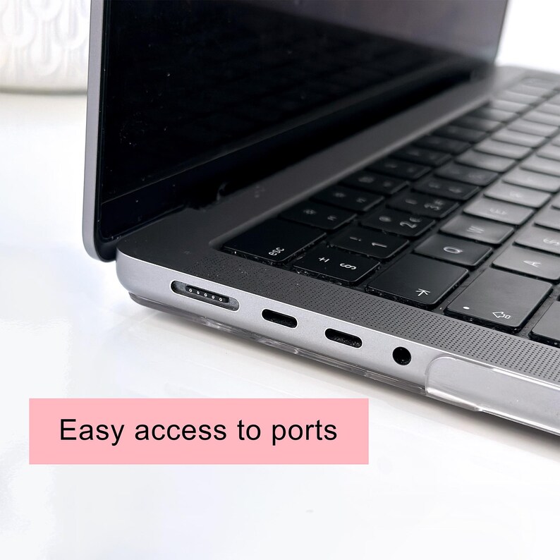 May include: A silver laptop with a black keyboard and a clear protective case. The side of the laptop features a magnetic charging port, two USB-C ports, and a headphone jack. A pink rectangular graphic with the text Easy access to ports is visible.
