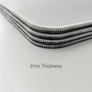May include: Close-up of three layers of white fabric with black stitching around the edges. The fabric is 2mm thick.