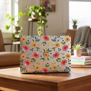 May include: A laptop skin featuring a watercolour pattern of pink and yellow flowers, green leaves, and small blue dots on a light background. The design covers the exterior surface of the laptop, showcasing a repeating floral motif.