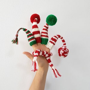 Puede incluir: Tres títeres de dedo con forma de gorro de elfo navideño. Los gorros son de rayas rojas y blancas con ribetes verdes y pompones.