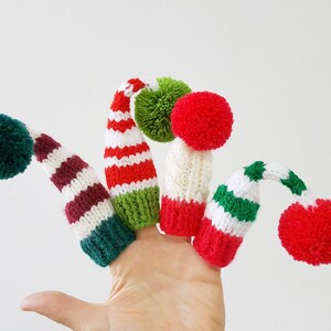 Puede incluir: Cinco marionetas de dedo con forma de gorros de Navidad con pompones. Los gorros son de rayas rojas, blancas y verdes con pompones blancos.