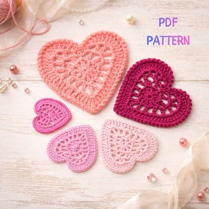 Puede incluir: Varios corazones de ganchillo en tonos rosados y rojos. Los corazones presentan diseños calados y están dispuestos sobre una superficie clara. El texto "PDF PATTERN" es visible en la imagen.