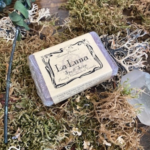 May include: A bar of purple soap with a brown paper label that reads "Madame Phoenix's La Luna Spell Soup Proudly Handmade in Canada" and "Use La Luna Spell Soap to connect with the endless tides of magic. This blend..."