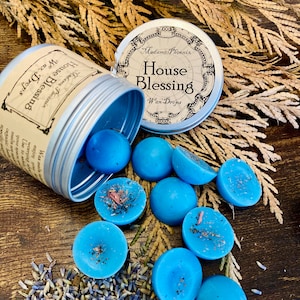 May include: A silver tin with a blue lid containing blue wax melts. The tin has a label that reads "Madame Phoenix House Blessing Wax Drops". The wax melts are scattered around the tin on a wooden surface.