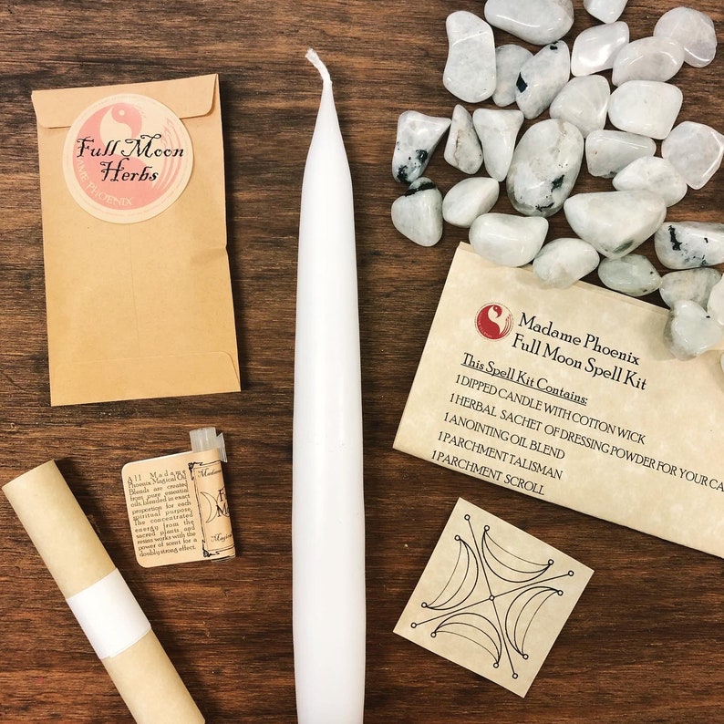 May include: A full moon spell kit with a white candle, a small brown pouch with the text "Full Moon Herbs", a small bottle of oil, a rolled parchment scroll, a parchment talisman with a moon symbol, and a bag of white moonstone crystals. The text on the bag reads "Madame Phoenix Full Moon Spell Kit. This Spell Kit Contains 1 Dipped Candle with Cotton Wick 1 Herbal Sachet of Dressing Powder for Your Ca 1 Anointing Oil Blend 1 Parchment Talisman 1 Parchment Scroll"
