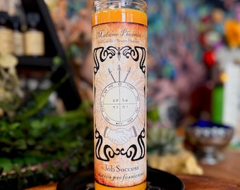 May include: A tall, cylindrical orange candle in a clear glass jar. The label features the text Madame Phoenix, Job Success, and a circular emblem with Hebrew characters, three arrows, and a pair of shaking hands, all set on a black saucer.