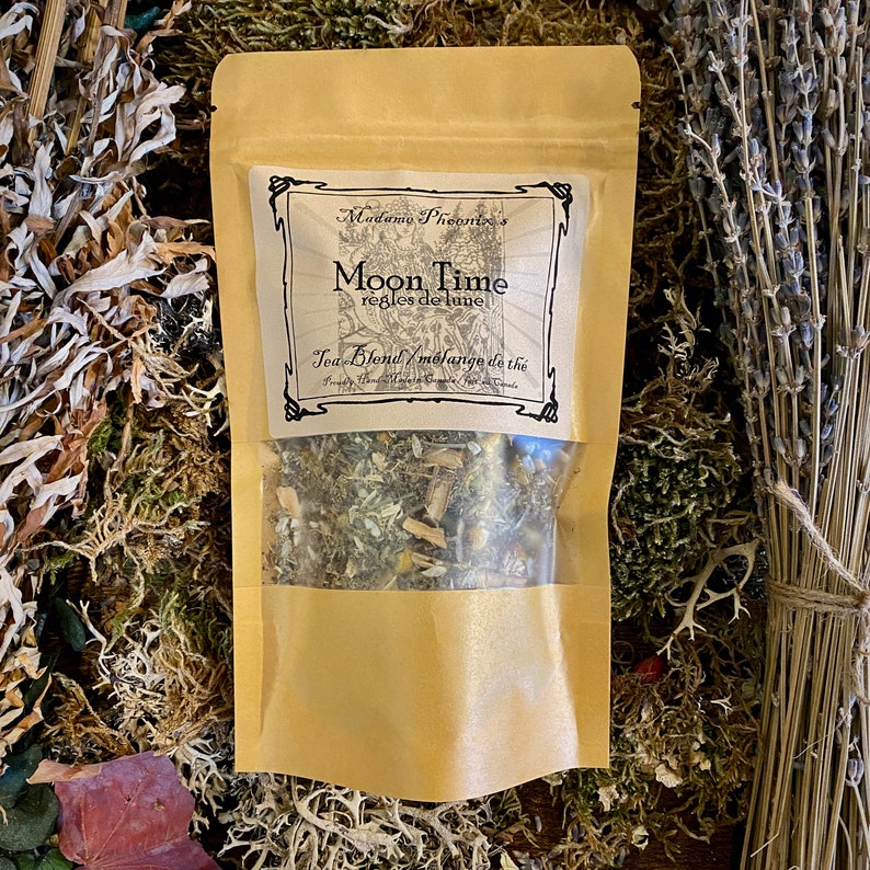 May include: A brown paper pouch with a clear window, containing a blend of dried herbs and flowers. The pouch has a label that reads "Madame Phoenix's Moon Time Regles de Lune Tea Blend Melange de the".