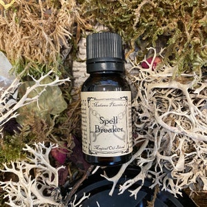 May include: A small brown glass bottle with a black cap. The label reads "Madame Phoenix's Spell Breaker Magical Oil Blend". The bottle is surrounded by dried moss.