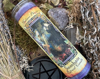 May include: Purple Samhain ritual candle with a label that says "Madame Phoenix" and features an illustration of three women standing around a cauldron. The candle is surrounded by dried herbs, moss, and crystals.