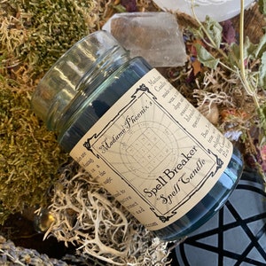 May include: A black spell breaker candle in a glass jar with a label that reads "Spell Breaker Spell Candle" and "Madame Phoenix's". The label also features a circular design with numbers and symbols.