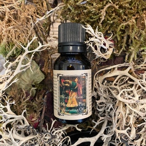 May include: A small brown glass bottle with a black cap. The label reads "Madame Picasso's Morgan le Fay Anointing Oil". The label also features an illustration of a woman in a red dress holding a staff.
