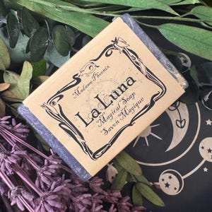 May include: A bar of La Luna Magical Soap, wrapped in clear cellophane. The soap's label is tan with black decorative script and the words "La Luna Magical Soap Savon Magique". The soap is surrounded by dried lavender and greenery.