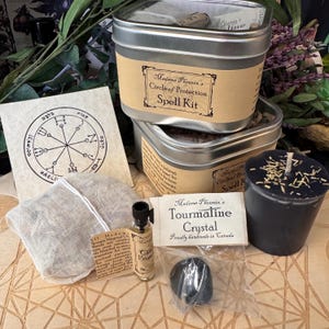 May include: A Madame Phoenix Circle of Protection spell kit in a silver metal tin, including a black candle with herbs, a small glass vial of oil, a black tourmaline crystal in a plastic bag, a white cloth pouch, and a card with a circular symbol.