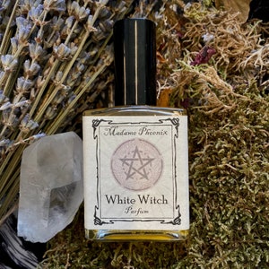 May include: A small glass bottle of perfume with a black cap. The label is white with black text that reads "Madame Phoenix" and "White Witch Parfum". A pentagram is featured on the label.