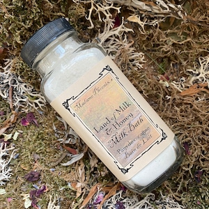 May include: A glass jar filled with white powder, labelled "Madame Phoenix's Land of Milk & Honey Milk Bath Pays de cocagne Bain de Lait".