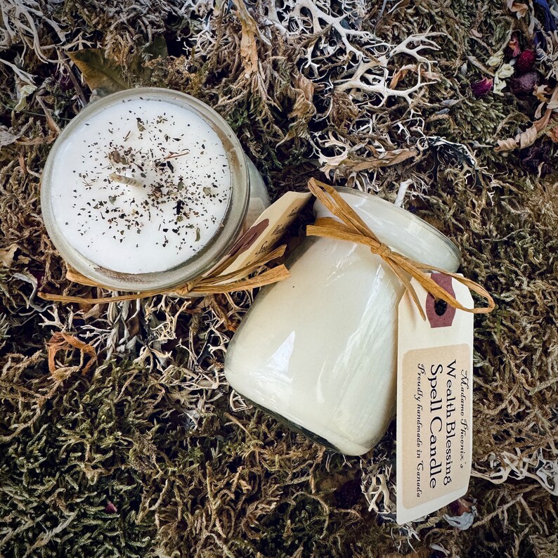 May include: Two glass candle jars with white wax and a brown label. The label reads "Wealth Blessing Spell Candle" and "Proudly handmade in Canada".