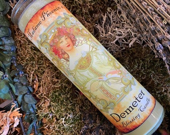 Op de afbeelding: Een gele kaars met een wit label waarop "Demeter Blessing Candle" staat en een vintage illustratie van een vrouw met bloemen in haar haar. Het label vermeldt ook "Madame Phoenix's".