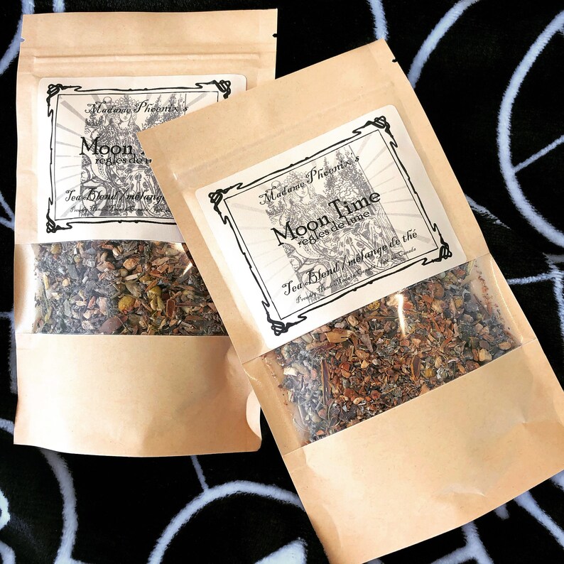 May include: Two brown paper bags with clear plastic windows showing loose leaf tea blends. The bags are labeled "Madame Pheoms's Moon Time" and "Madame Pheoms's Moon" with the text "regles de lune" and "Tea Blend/melange du the" in black and white.