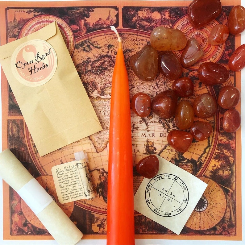 May include: A flat lay of a red candle, a small brown envelope with the text "Open Read Herbs" and a white label with the text "All Madams Phoenix Magical Oil", a small brown scroll, a small white label with Hebrew text, and a collection of carnelian stones on a vintage world map background.