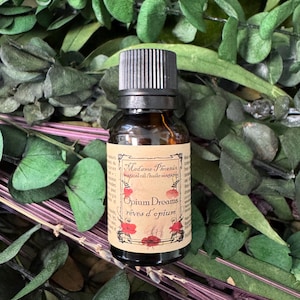 Könnte beinhalten: Eine kleine bernsteinfarbene Glasflasche mit schwarzem geripptem Verschluss und beigem Etikett. Das Etikett zeigt den Text Madame Phoenix magical oil, Opium Dreams und rèves d'opium, verziert mit roten Mohnblumen und schwarzen Rahmen.
