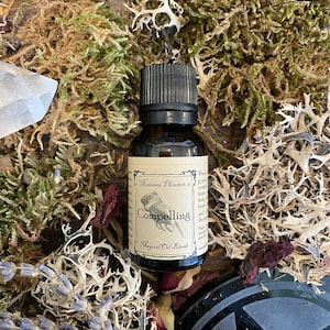 May include: A small brown glass bottle with a black cap. The label reads "Madame Phoenix's Compelling Magical Oil Blend".