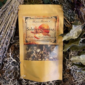 May include: A brown paper bag with a clear window showing a blend of mulling spices. The bag has a label that reads "Madame Phoenix's Solstice Blessing bénédiction du solstice Mulling spice blend/épices à fondre Proudly Hand Made in Canada/fait au Canada".